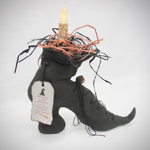May include: A black fabric boot-shaped decoration filled with orange and black raffia, featuring a battery-operated candle, a small bell, and a hanging tag printed with the text: When witches go riding, and black cats are seen, the moon laughs and whispers, 'tis near Halloween.