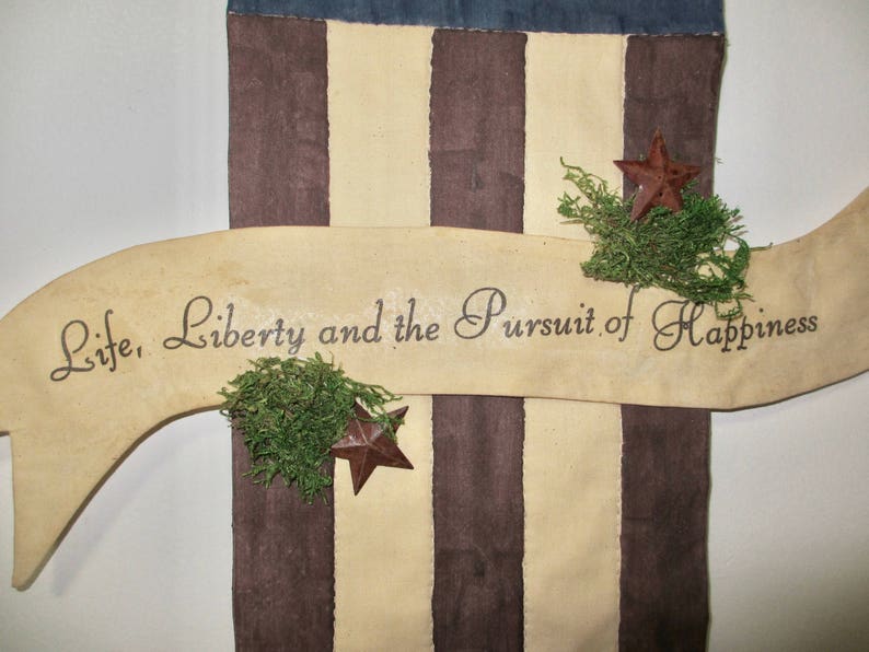 May include: A decorative banner with a brown, white, and blue striped background. The banner has a white ribbon with the text "Life, Liberty and the Pursuit of Happiness" written in black. The ribbon is curved and has a brown star at the end.