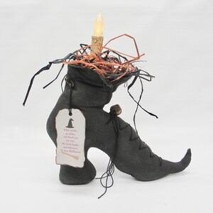 May include: A black witch's boot with a lit candle inside, surrounded by straw and black string. A tag attached to the boot reads "When witches go riding, and black cats are seen, the moon laughs and whispers, It's near Halloween."