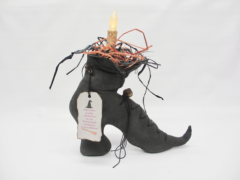 May include: A black witch's boot with a lit candle inside, surrounded by straw and black string. A tag attached to the boot reads "When witches go riding, and black cats are seen, the moon laughs and whispers, It's near Halloween."