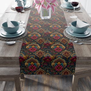 May include: A decorative table runner with a dark background and a repeating floral pattern in shades of red, blue, yellow, and brown. The runner is placed on a wooden table set for a meal, with plates, glasses, and silverware.