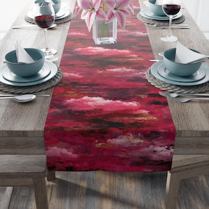 Może przedstawiać: Żywy czerwony bieżnik z wzorem przypominającym chmury w odcieniach czerwieni, czerni, bieli i złota. Bieżnik jest umieszczony na drewnianym stole nakrytym do posiłku, z talerzami, miskami, sztućcami i kieliszkami do wina.