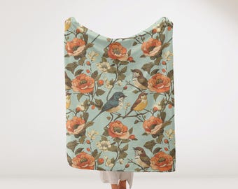 May include: A teal blue throw blanket with a floral pattern featuring orange, pink, and yellow flowers and blue and yellow birds.