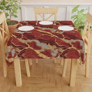 May include: A rectangular tablecloth with a red, gray, and gold marble pattern. The tablecloth is set on a wooden table with four white plates, knives, and forks. The table is surrounded by wooden chairs.