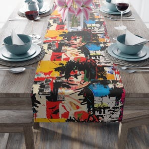 Peut inclure: Une nappe colorée avec un motif abstrait aux éclaboussures audacieuses de rouge, jaune, bleu et noir. L'œuvre d'art semble être un collage ou une impression inspirée du graffiti. La nappe est posée sur une table en bois dressée pour un repas.