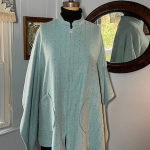 May include: A light blue cape-style jacket with a gold zipper and two large front pockets. The jacket has a subtle dotted pattern and is displayed on a mannequin. The jacket is a unique outerwear piece.