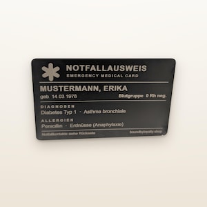 Könnte beinhalten: Eine rechteckige schwarze Notfallausweis-Karte mit weißem Text. Sie zeigt das Stern-der-Lebens-Symbol, den Namen MUSTERMANN, ERIKA, das Geburtsdatum 14 03 1978, die Blutgruppe 0 Rh neg., Diagnosen Diabetes Typ 1 und Asthma bronchiale sowie Allergien gegen Penicillin und Erdnüsse.