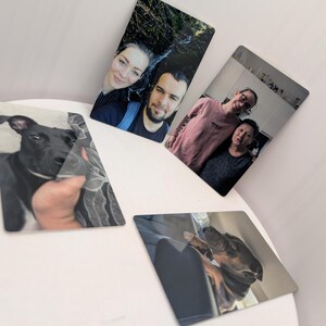 K&ouml;nnte beinhalten: Vier rechteckige Fotoabz&uuml;ge mit verschiedenen Motiven: ein schwarzer Hund, ein Paar im Freien, zwei Personen in einem Innenraum und ein Hund, der in einem Fahrzeug ruht. Die Abz&uuml;ge liegen auf einer wei&szlig;en Fl&auml;che mit dem Text PARTNER. FAMILIE. HAUSTIER.