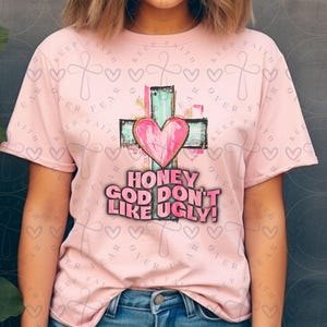 Könnte beinhalten: Rosa T-Shirt mit einem Grafikdruck eines Herzens auf einem Kreuz und dem Text "Honey God Don't Like Ugly!"
