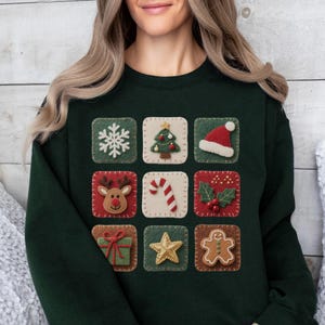 May include: Dark green sweatshirt with nine festive Christmas-themed squares. Each square displays a different design, such as a snowflake, Christmas tree, Santa hat, reindeer, candy cane, holly, gift, star, and gingerbread man.