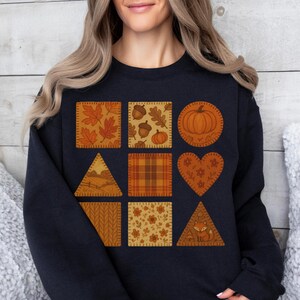 Könnte beinhalten: Ein schwarzes Sweatshirt mit neun herbstlichen Aufnähern in Orange, Braun und Gelb. Die Aufnäher zeigen Blätter, Eicheln, Kürbisse und einen Fuchs. Ein gemütliches Herbstmode-Teil.