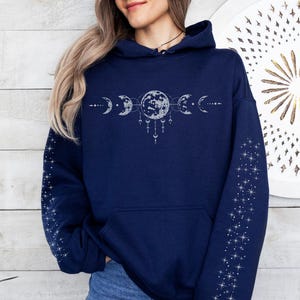 May include: Navy blue hooded sweatshirt with a celestial design. The design features phases of the moon and stars on the sleeves. The sweatshirt is a comfortable, casual garment.