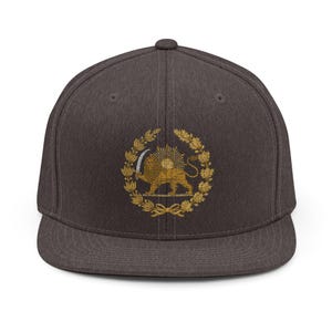 Op de afbeelding: Een donkergrijze pet met platte klep en een goud geborduurd embleem. Het embleem toont een leeuw met een zwaard, omringd door een krans en een zonnestraal, met een strik aan de onderkant. De pet heeft een gestructureerde pasvorm.