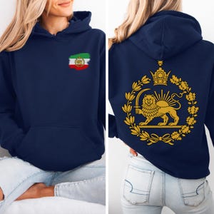May include: Navy blue hoodie with a front pocket and a hood. The front features a small Iranian flag design. The back displays a gold emblem of a lion holding a sword, surrounded by a wreath and crown. The hoodie is made of a soft material.