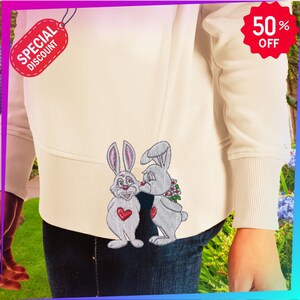 May include: Cream-colored hoodie with embroidered cartoon bunnies. One bunny has a red heart on its chest, the other is kissing it. The hoodie has a ribbed hem and cuffs. A red tag reads "SPECIAL DISCOUNT" and a red starburst reads "50% OFF".