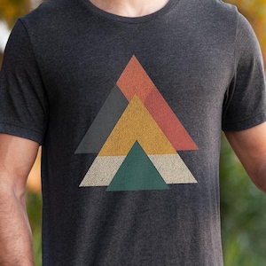 May include: A dark heather grey t-shirt with a geometric design featuring a series of overlapping triangles in shades of orange, yellow, green, and blue.