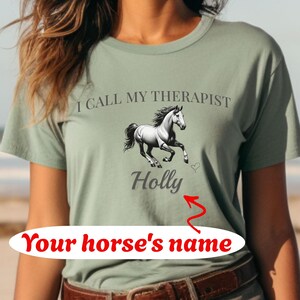 Op de afbeelding: Groen T-shirt met een witte paard afbeelding en de tekst "Ik noem mijn therapeut Holly". De tekst "De naam van je paard" staat onder de naam Holly.