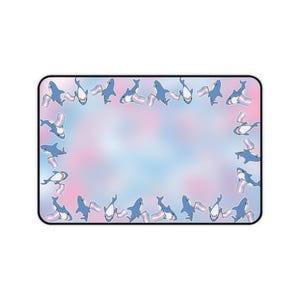 May include: Rectangular mouse mat with a pastel pink, blue, and white background. The border features blue cartoon sharks holding a transgender pride flag. The mouse mat has a black border.