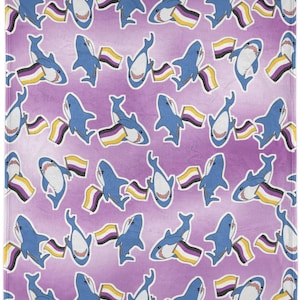 May include: A purple blanket featuring a repeating pattern of blue cartoon sharks holding non-binary pride flags. The sharks have white bellies and open mouths. The flags are yellow, white, purple, and black.