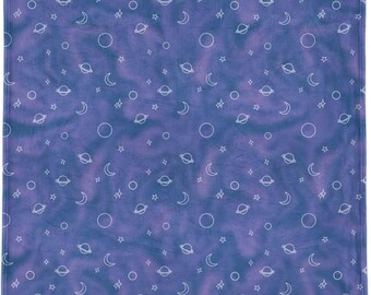 Puede incluir: Una manta cuadrada morada con un patrón celestial. El diseño presenta contornos blancos de planetas, lunas, estrellas y círculos dispersos sobre un fondo teñido anudado. La manta es un textil suave y acogedor.
