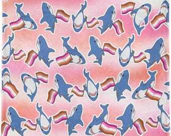 Op de afbeelding: Een roze en oranje gradiënt achtergrond is bedekt met een patroon van blauwe cartoon haaien die lesbische pride vlaggen vasthouden. De haaien hebben witte buiken en open monden met zichtbare tanden. De vlaggen hebben roze, oranje en bruine strepen.