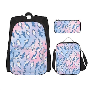 May include: A black backpack, pencil case, and lunch bag set. Each item features a repeating pattern of blue sharks on a pastel pink and blue gradient background. The backpack has a front pocket and mesh side pockets.