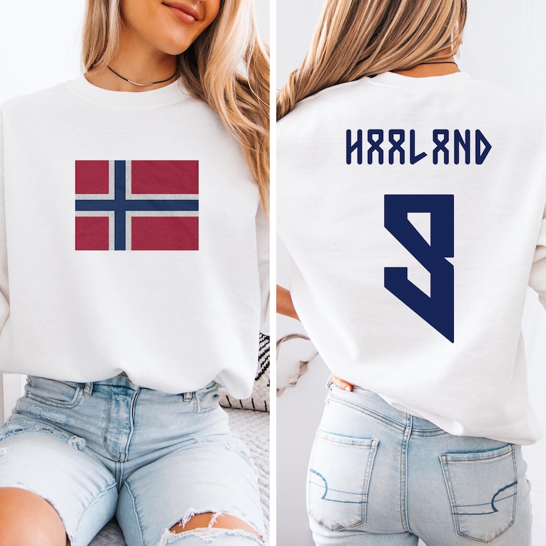 A woman wearing a white sweatshirt with the Norwegian flag and the number 9 on the back, as well as a pair of blue jeans.