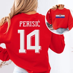 A woman wearing a red sweatshirt with the number 14 and the word "PERISIC" printed on it.