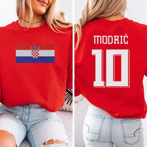 A woman wearing a red shirt with the Croatia national flag and the number 10 on it, as well as a jersey with the name "Modric" and the number 10 on it.