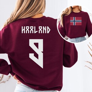 A woman wearing a burgundy sweatshirt with the name 'Hålnd' and the number '9' printed on it.