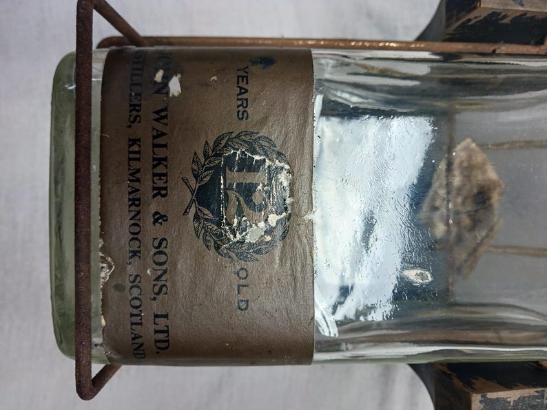 May include: A clear glass bottle with a brown label that reads "John Walker & Sons, Ltd. Distillers, Kilmarnock, Scotland" and "15 Years Old." The bottle is held in a metal cage.