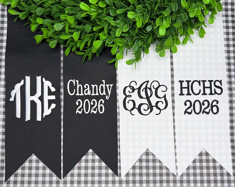 May include: Four vertical fabric pennants with swallowtail ends, two black and two white. The black pennants feature white embroidery of the letters TKE and the text Chandy 2026. The white pennants feature black embroidery of the letters EGG and HCHS 2026.