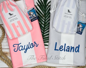 May include: Two quick-dry beach towels with matching drawstring bags. One towel is pink with white stripes and the name "Taylor" embroidered in blue. The other is gray with white stripes and the name "Leland". Both have "Dock & Bay" branding.