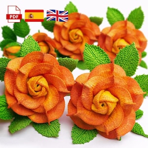 Puede incluir: Primer plano de varias rosas de ganchillo naranjas y amarillas con hojas verdes. Las rosas tienen detalles de pétalos y un aspecto texturizado. La imagen incluye un icono PDF, la bandera española y la bandera británica.