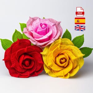 Puede incluir: Tres rosas de ganchillo en rojo, rosa y amarillo, con hojas verdes. Las rosas tienen pétalos detallados y en capas, y las hojas tienen un aspecto texturizado. La imagen incluye un icono PDF y banderas.
