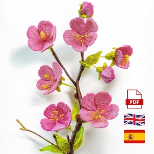 Puede incluir: Una rama floral de ganchillo con flores rosas y centros amarillos, hojas verdes y tallos marrones. La imagen muestra varias flores abiertas y capullos. El fondo es blanco. También se ve un icono PDF, una bandera británica y una bandera española.