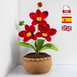 Puede incluir: Una planta de orquídeas hecha a mano con flores rojas vibrantes y centros amarillos. La planta tiene hojas verdes y está en una maceta de ganchillo marrón. La imagen incluye un icono PDF, la bandera española y la bandera británica.
