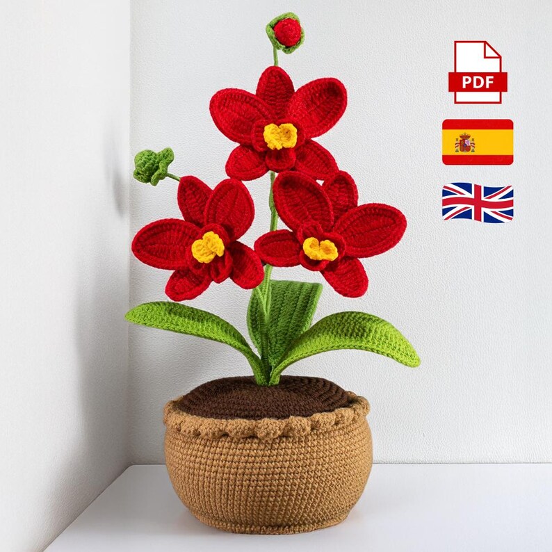 May include: A handcrafted crochet orchid plant with vibrant red flowers and yellow centers. The plant features green leaves and is potted in a brown crochet pot. The image includes a PDF icon, the Spanish flag, and the British flag.