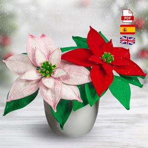 Puede incluir: Dos flores de pascua de ganchillo en un jarrón plateado. Una flor es roja, la otra rosa, con hojas verdes. La imagen incluye un icono PDF, una bandera española y una bandera británica.