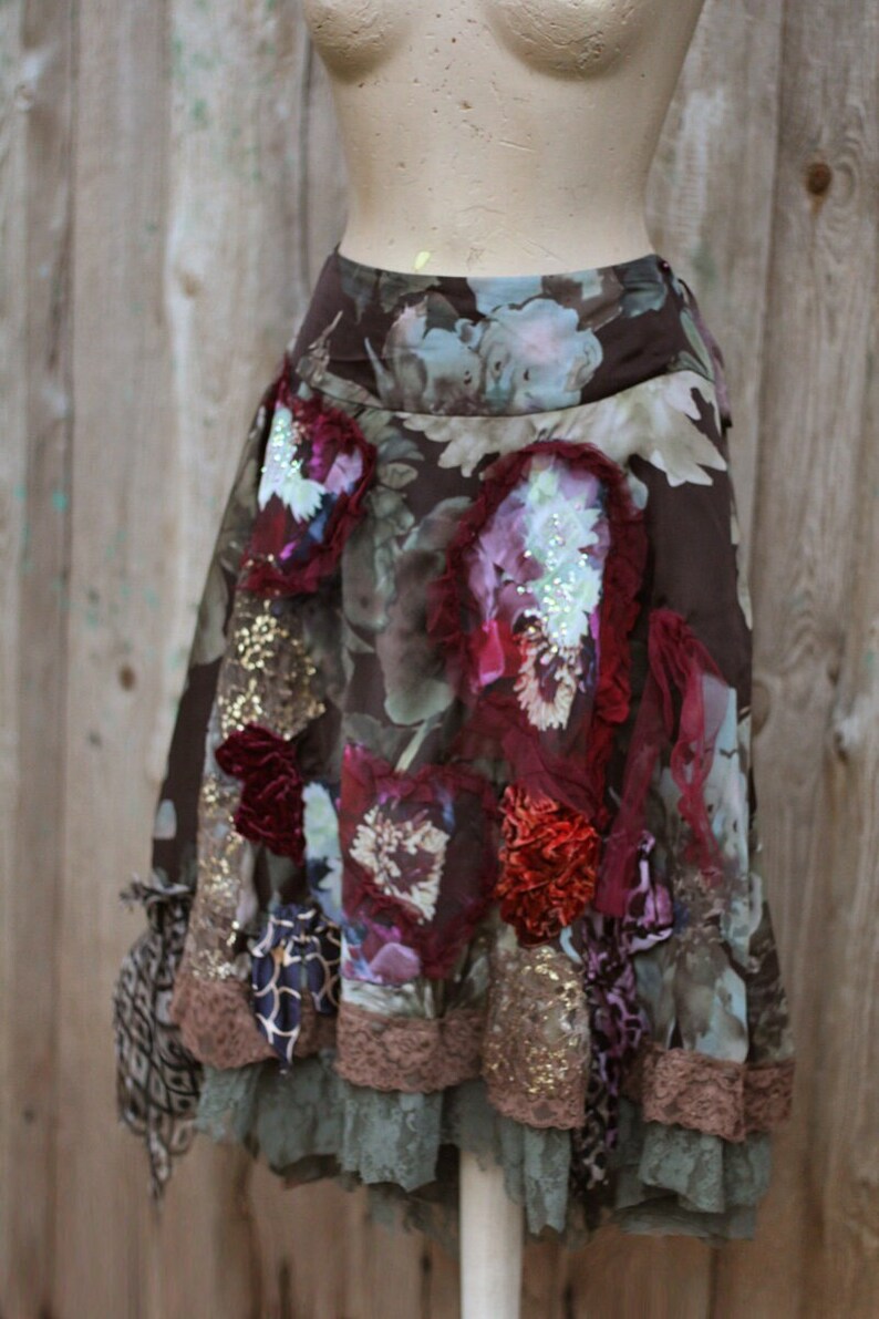 May include: A brown, green, and burgundy floral skirt with a lace trim and embellishments. The skirt is made of a soft, flowing fabric and has a relaxed fit.