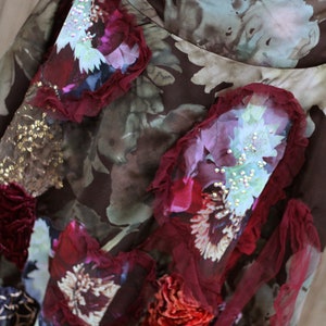 May include: A brown skirt with a floral print and layered fabric embellishments. The skirt features a variety of colors, including red, pink, and gold. The fabric is textured and has a vintage feel.