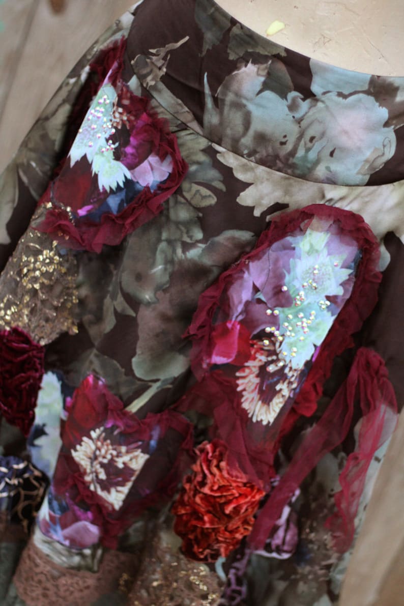 May include: A brown skirt with a floral print and layered fabric embellishments. The skirt features a variety of colors, including red, pink, and gold. The fabric is textured and has a vintage feel.