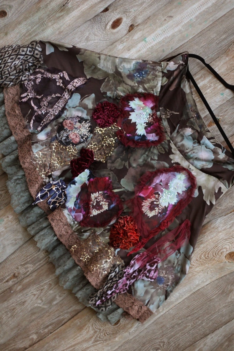 May include: A brown skirt with a floral print and layered ruffles. The skirt is decorated with sequins, lace, and velvet flowers.