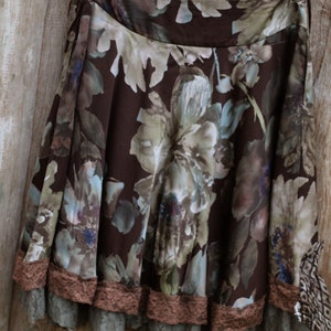 May include: A brown floral skirt with a lace trim. The skirt has a brown background with a floral pattern in shades of brown, green, and blue. The lace trim is a light brown color.
