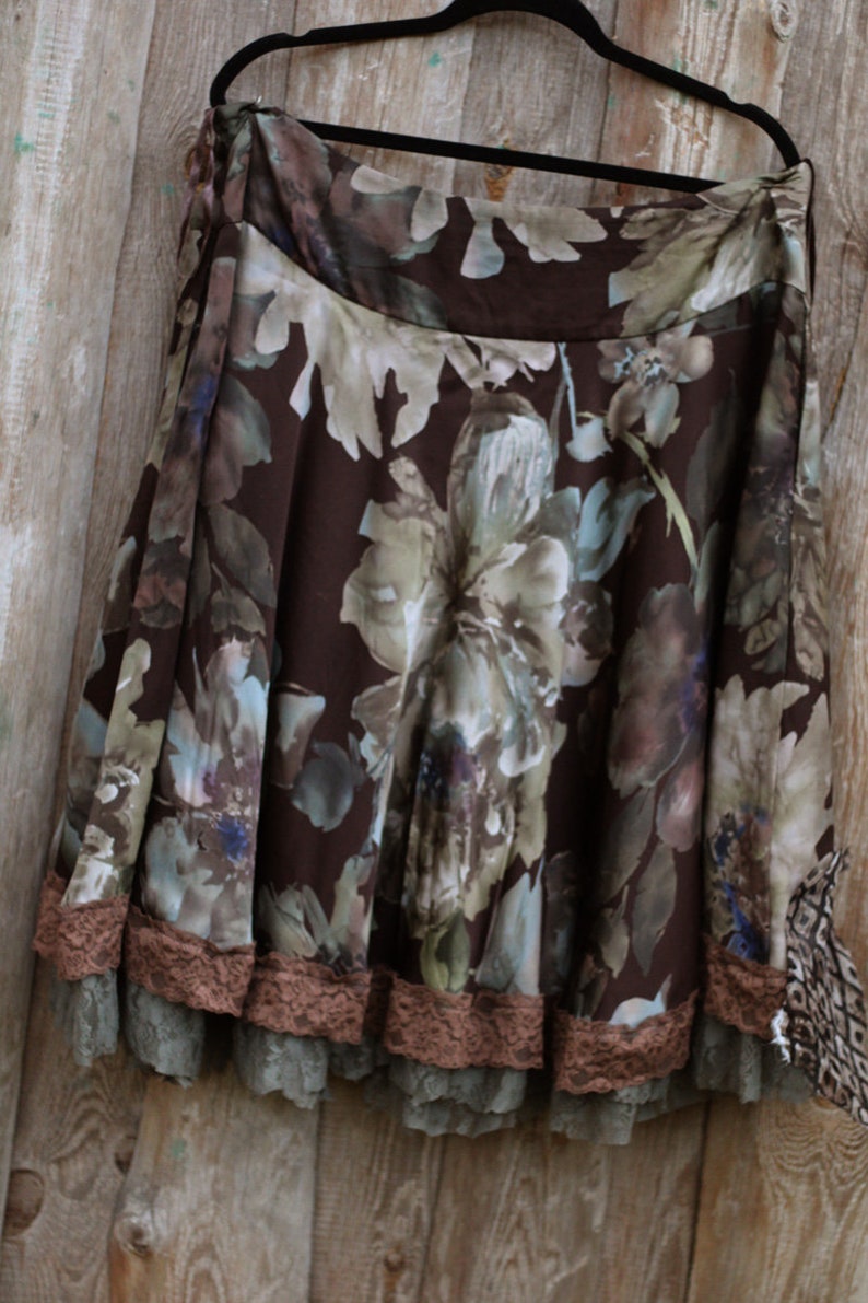 May include: A brown floral skirt with a lace trim. The skirt has a brown background with a floral pattern in shades of brown, green, and blue. The lace trim is a light brown color.