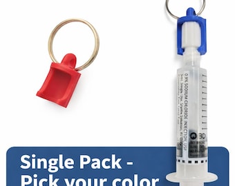 May include: A clear syringe with a blue and white cap attached to a keyring, and a red plastic keychain. The syringe has text that reads "0.9% SODIUM CHLORIDE INJECTION, USP". The text "Single Pack - Pick your color" is on a blue banner.