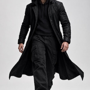 May include: A long black hooded trench coat worn over a black hooded sweatshirt and black cargo pants. The outfit is completed with black boots. The ensemble features a monochromatic black color scheme with a structured, layered appearance.