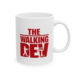 May include: White ceramic mug with a red graphic that reads "THE WALKING DEV". The design includes a zombie figure and a computer screen icon. The mug has a curved handle.