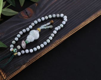 May include: A jade bead necklace with a gourd-shaped pendant. The necklace features small, round, light green beads and a larger, intricately carved pendant. The pendant is light green and white, with gold accents. The necklace is displayed on a dark wooden surface.