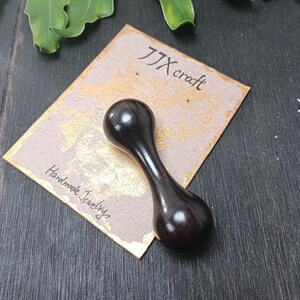 May include: A dark brown, hourglass-shaped wooden object, possibly a jewelry tool or a decorative item. The object is smooth and polished, with a bulbous top and bottom connected by a narrower midsection. The item rests on a card with the text "JJX craft" and "Handmade Jewelry".